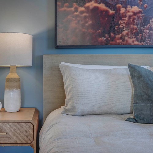 Detail of a model bedroom at our apartments in Salt Lake, Utah, featuring a blue wall and beige colored bedspread.