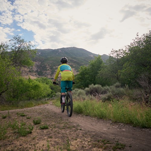 Photograph of someone riding a bicycle near our apartments in Daybreak Utah. They trail is through scrub brush and hills.