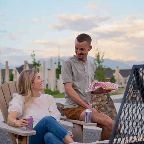 Two people sitting at an outdoor fireplace at our apartments in Daybreak, Utah. They are sitting on outdoor chairs. 