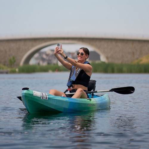 Photograph of someone taking a photograph of themself while sitting on a kayak in the river near our apartments in Daybreak. 