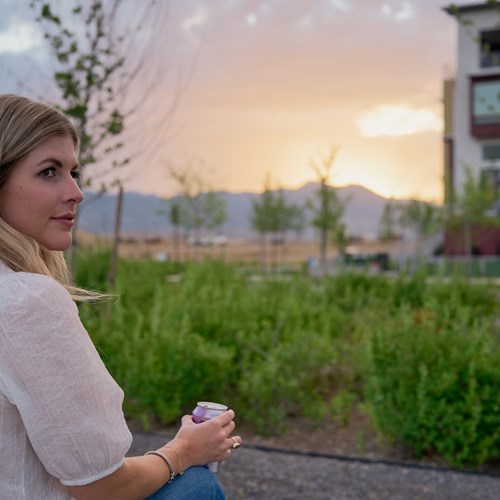 Photograph of someone looking at a sunset on the apartment grounds in Daybreak, Utah. She is holding a drink.