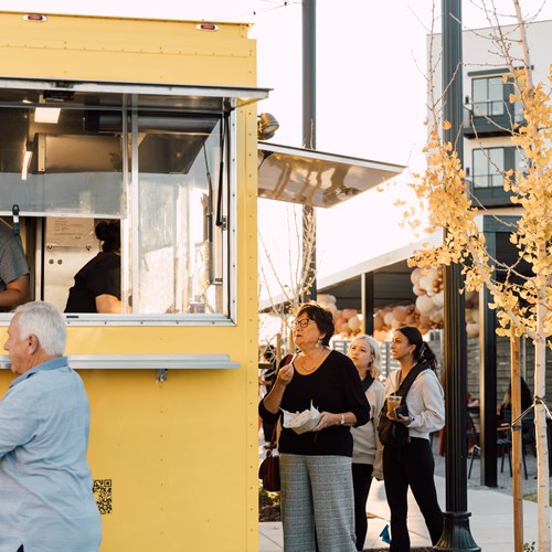 group of people ordering food from a yellow foodtruck