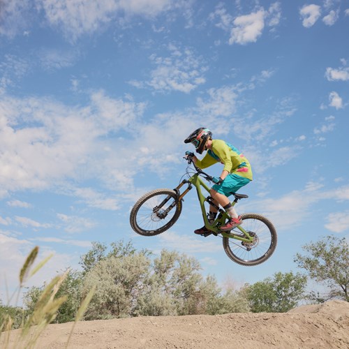 Photograph of someone riding a bmx bike off a jump. They are wearing a helmet and suspended in mid air 