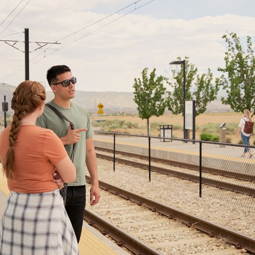 Photograph of two people standing at a train station near our apartments in Daybreak, Utah. The two people are talking. 